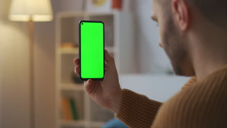 video-conferencing-by-smartphone-man-is-holding-gadget-with-green-screen-sitting-at-home-online-work-or-friendly-meeting-closeup-view-of-cell-phone